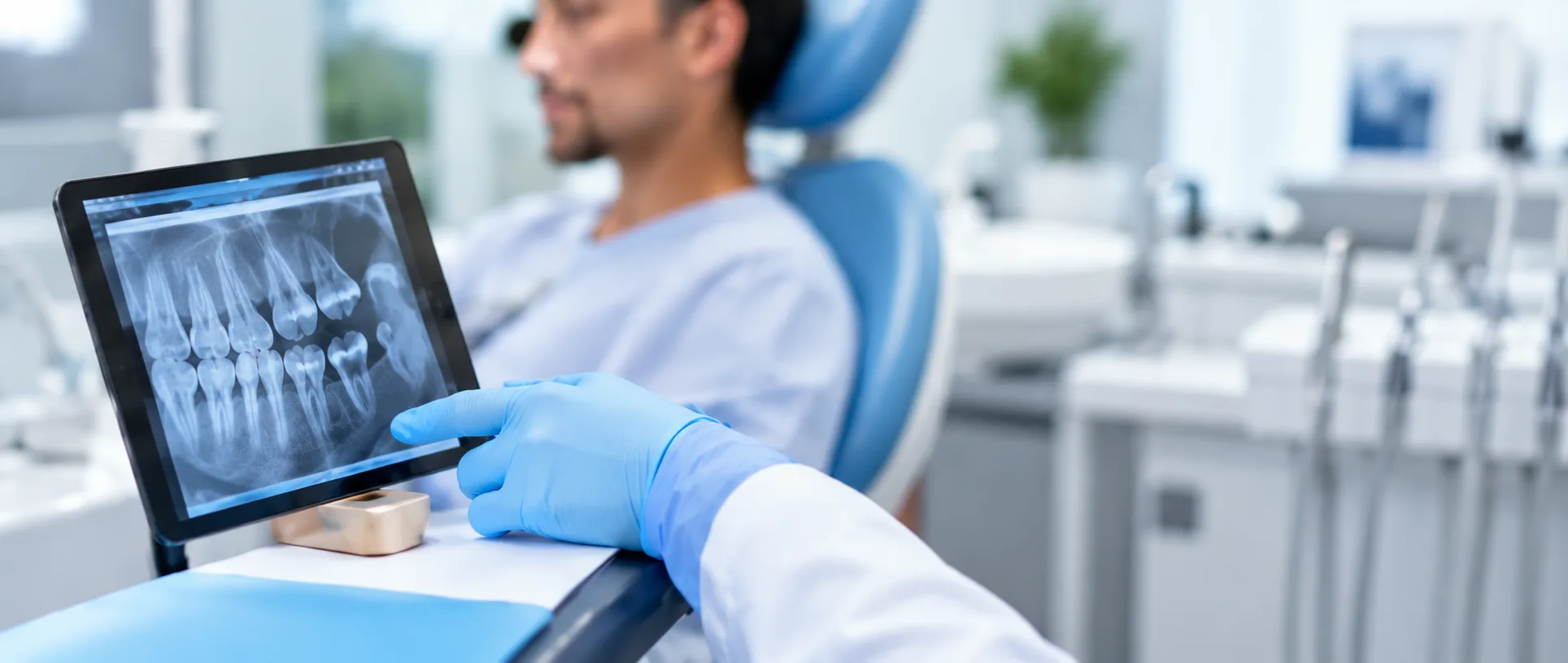 Dentist in blue gloves showing a patient a dental X-ray on a tablet